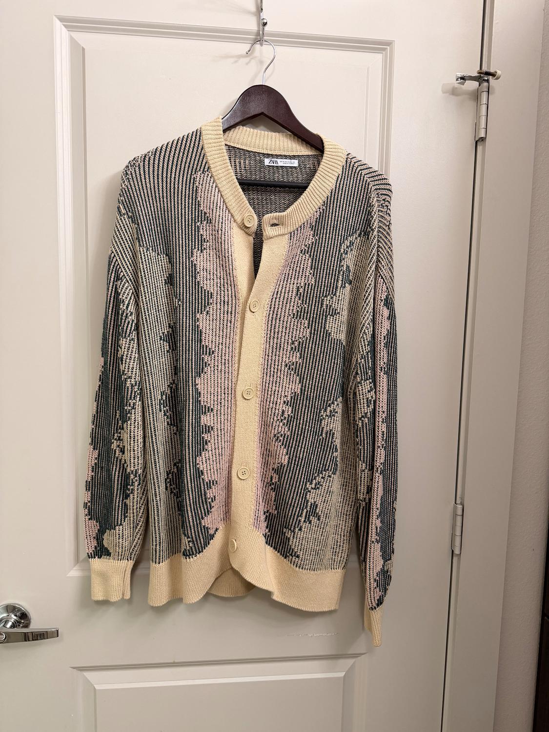 Cardigan hanging on a door, with a striped design and abstract patterns in beige, pink, and black tones. Visible label on the collar.