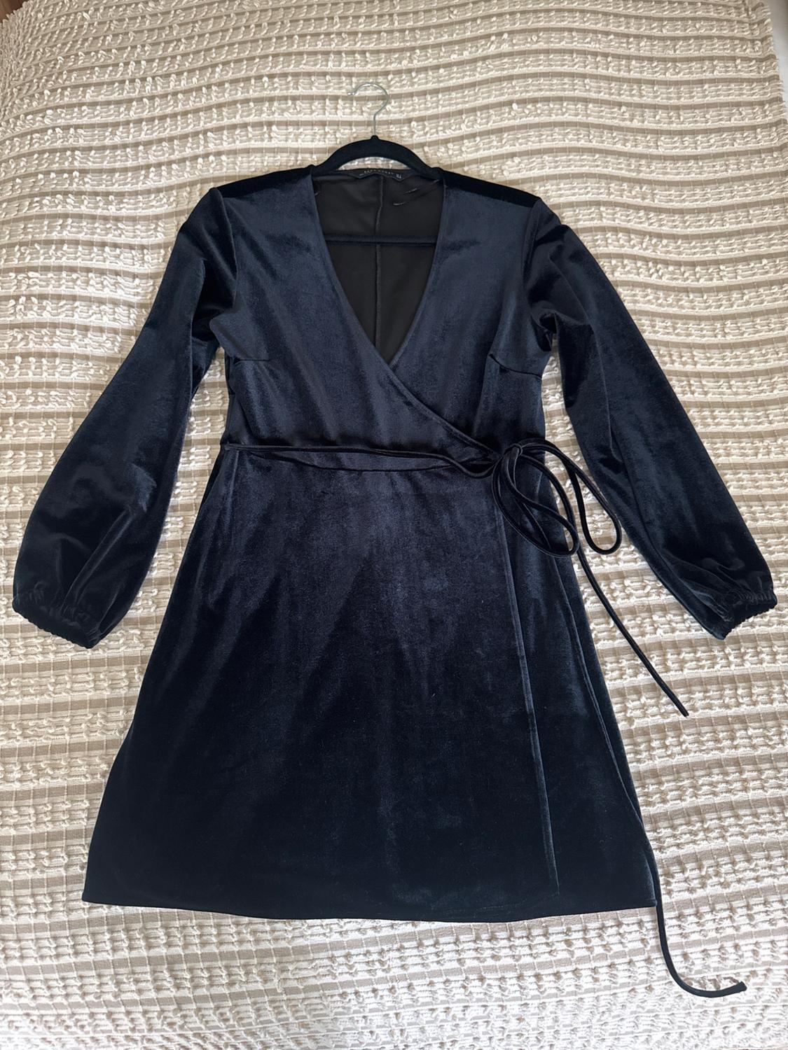 Black velvet dress with a V-neck and long sleeves, hanging over a bed with a woven textured bedspread.