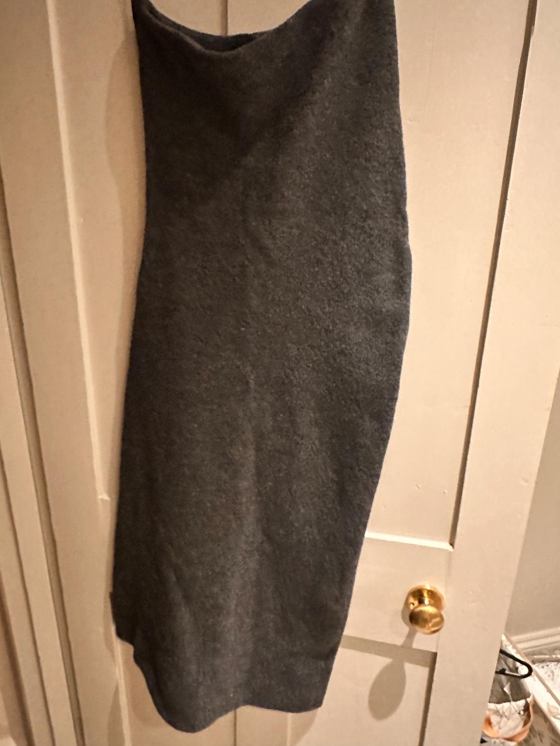 Long grey skirt hanging on a light wooden door with a gold handle. Background with floor and wall details.