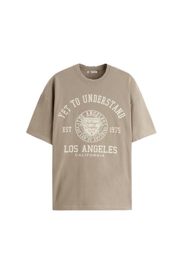 Μπεζ μπλουζάκι με κείμενο "YET TO UNDERSTAND", "LOS ANGELES CALIFORNIA", και "EST 1975" σε λευκό, πάνω σε λευκό φόντο.