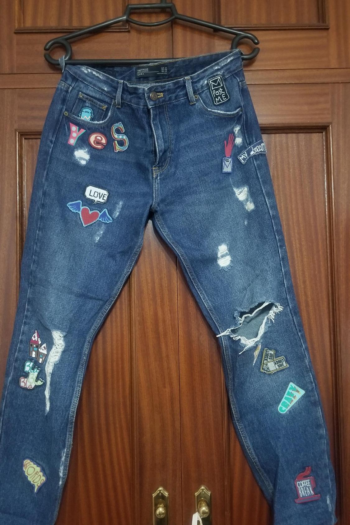 Front view of jeans with patches and rips, text 'LOVE', 'Post ME', 'YES', 'COFFEE BREAK', 'ADMIT ONE', 'NYC DREAM'.