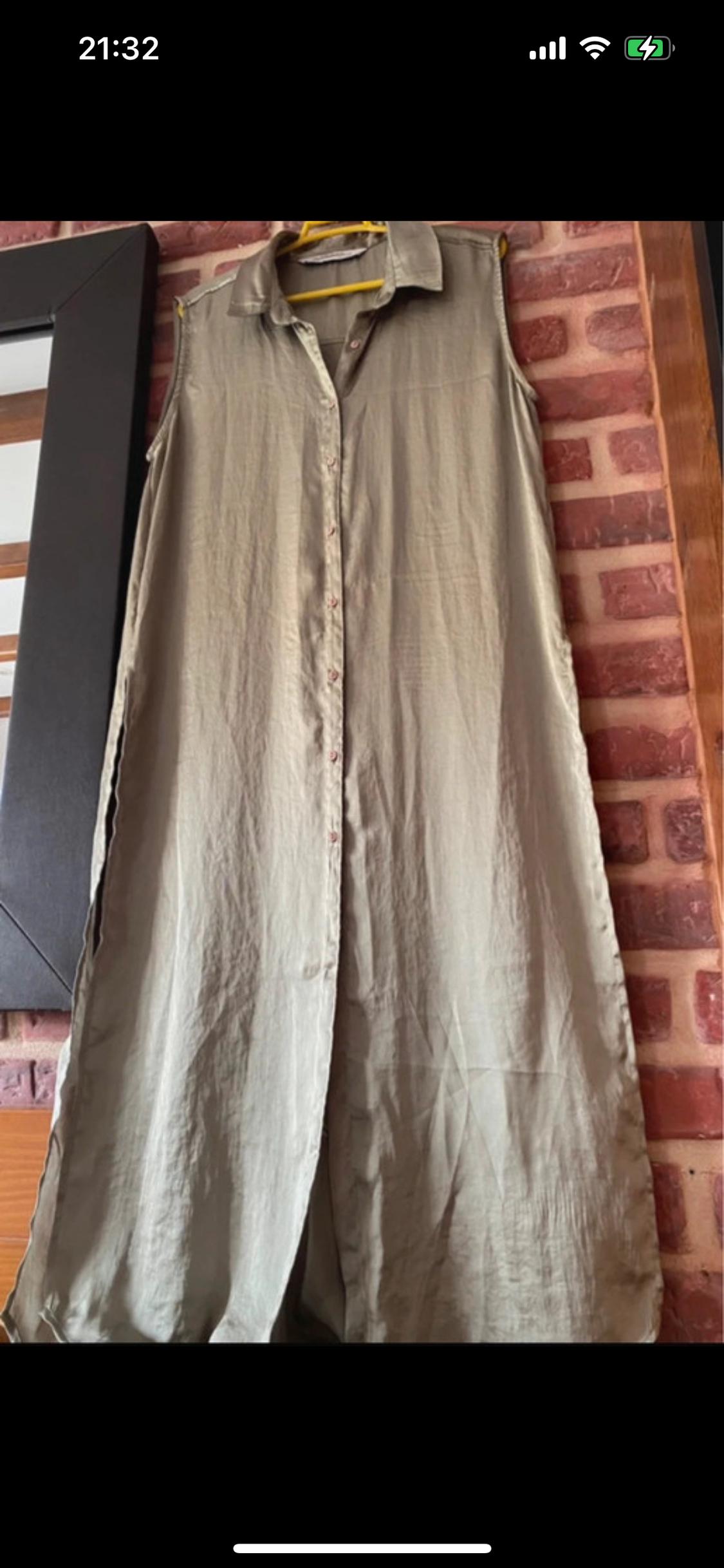 Beige sleeveless maxi dress hanging on a yellow hanger, with a red brick wall background.
