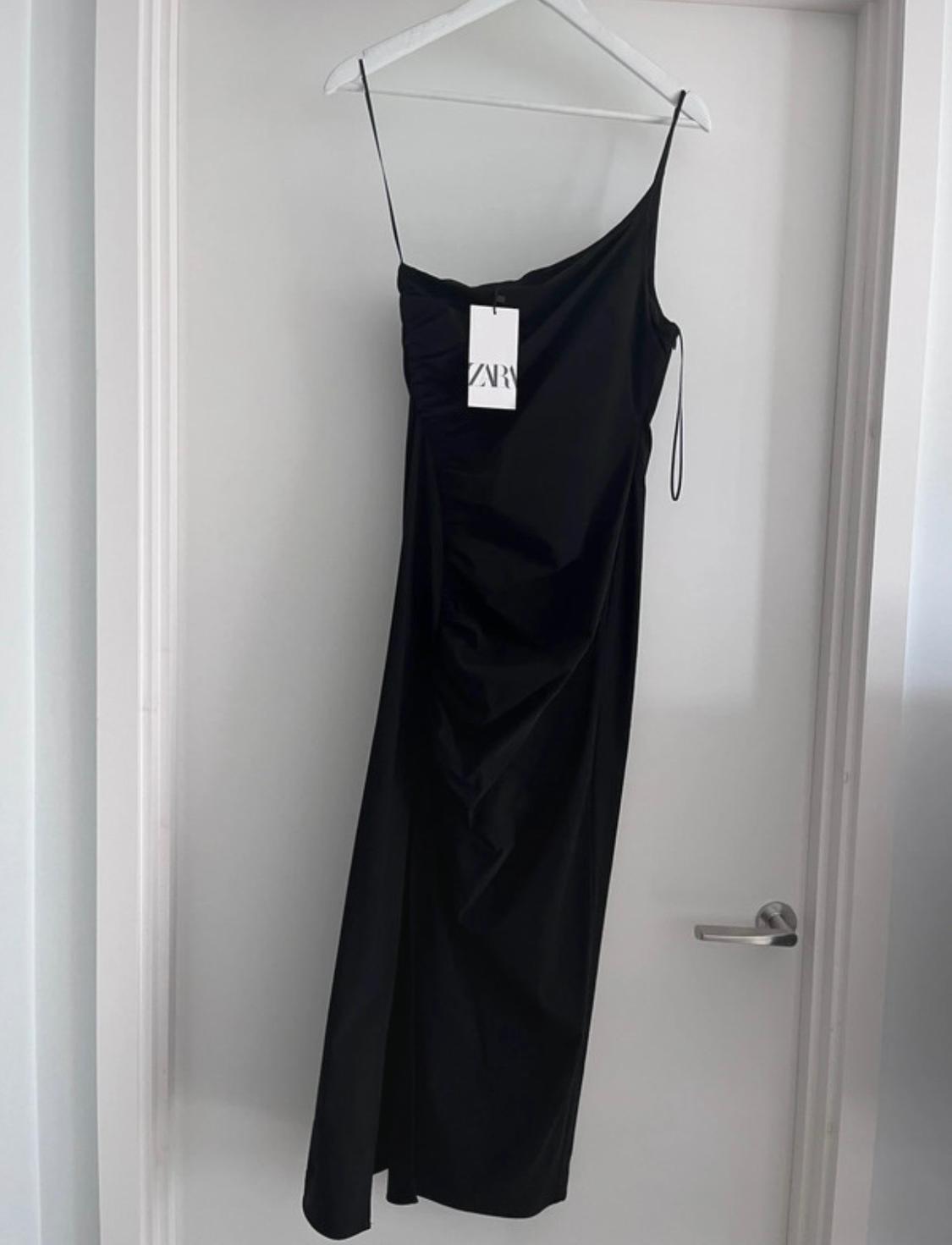 Black slip dress hanging on a white hanger over a door. Visible label with the text "ZARA".