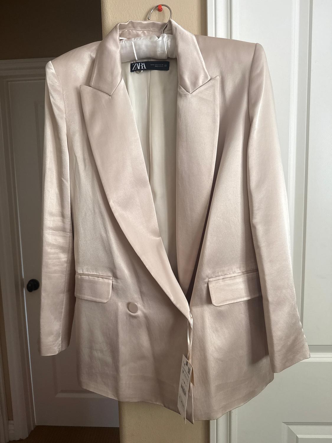 Beige satin jacket hanging on a hanger, with wide lapels and two front pockets. Visible Zara tag.