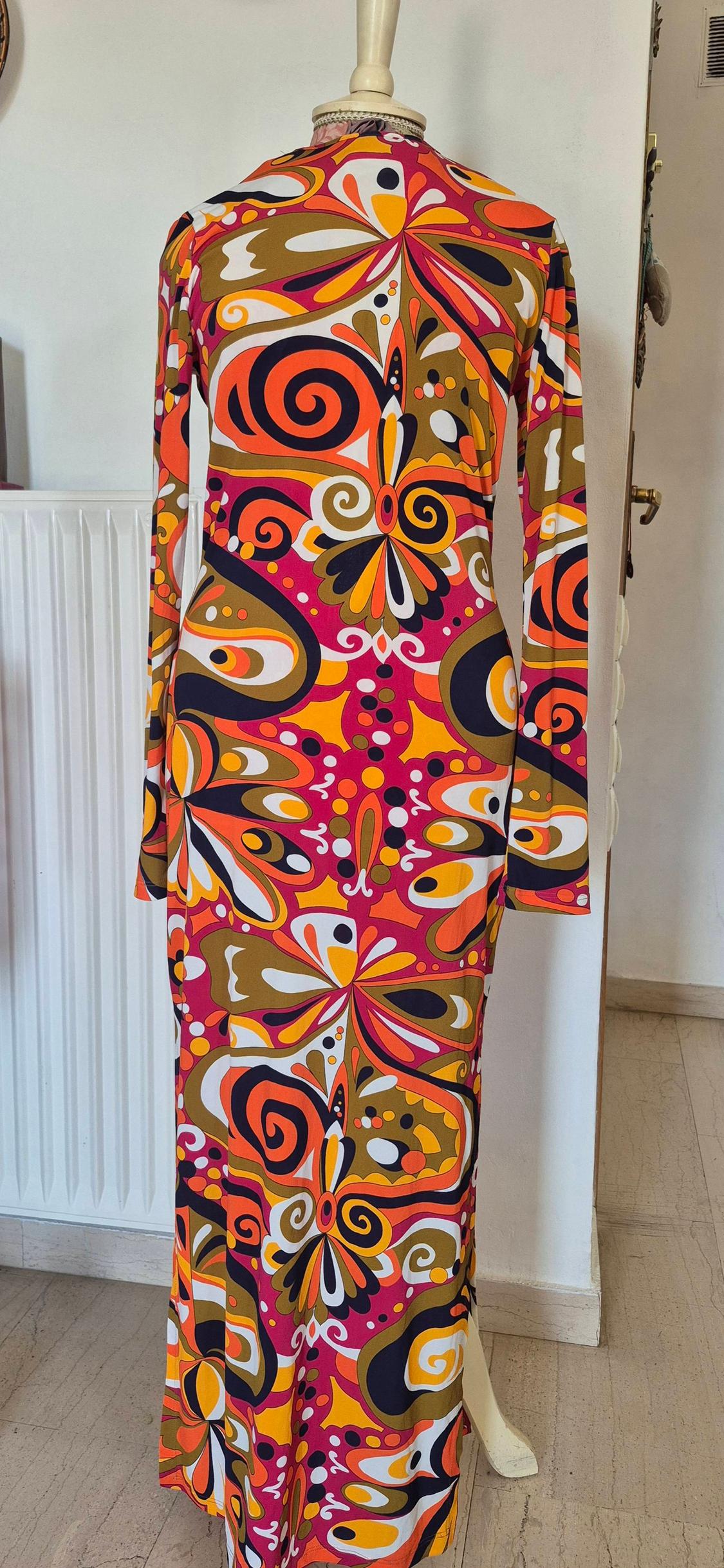 Long dress with a psychedelic print in shades of orange, pink, and brown, displayed on a mannequin in a bright interior.