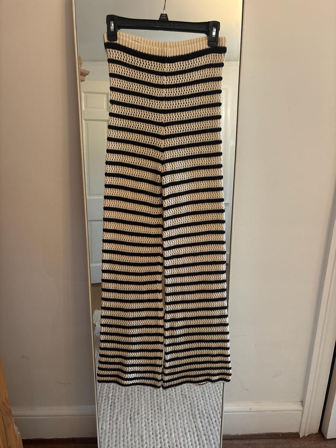 Black and beige horizontal striped knit trousers, hanging on a hanger in front of a mirror leaning against the wall.