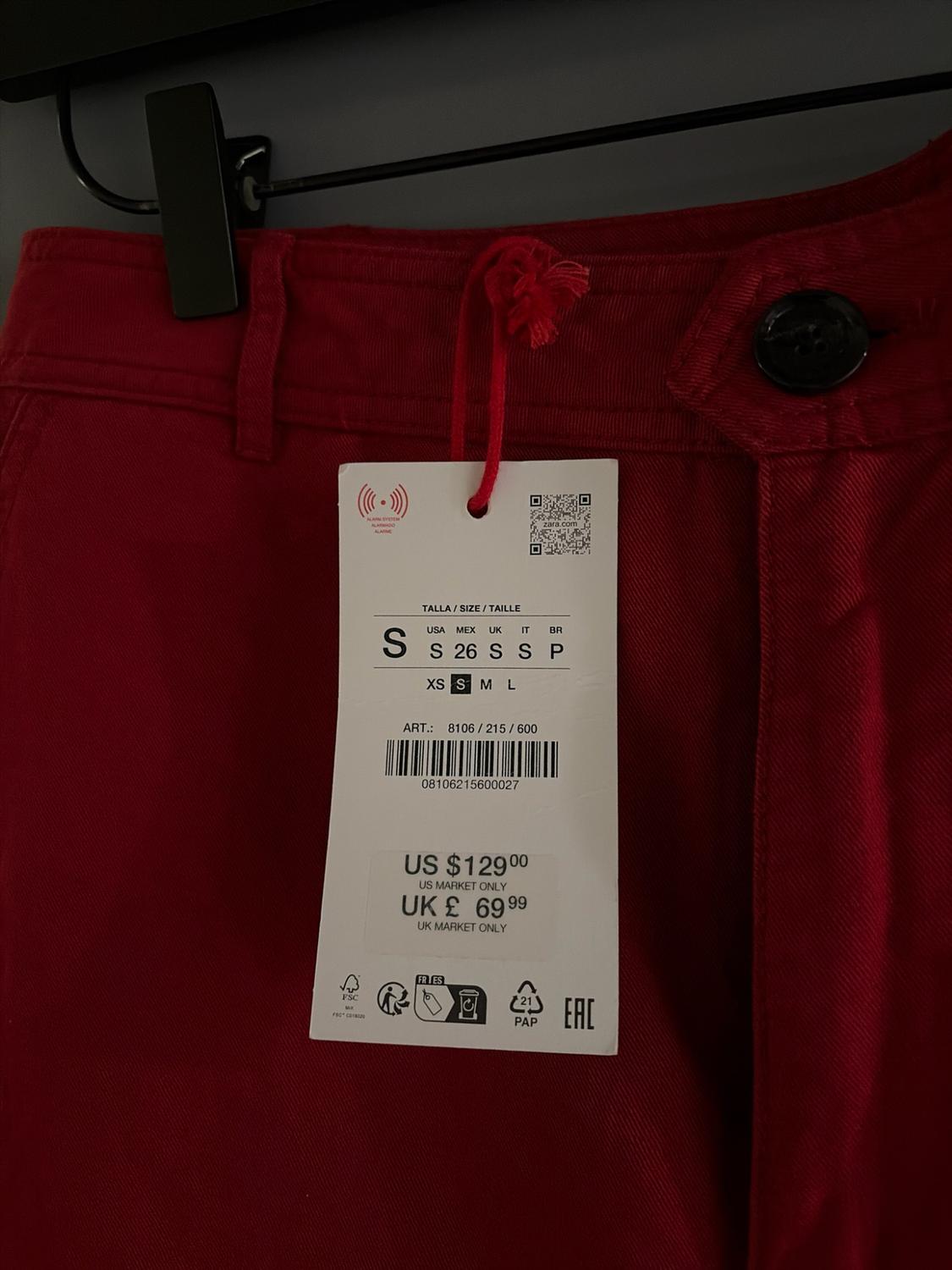 Red garment detail with button and label. Text: SIZE / SIZE / SIZE S, US $129.00 US MARKET ONLY, UK £ 69.99 UK MARKET ONLY.