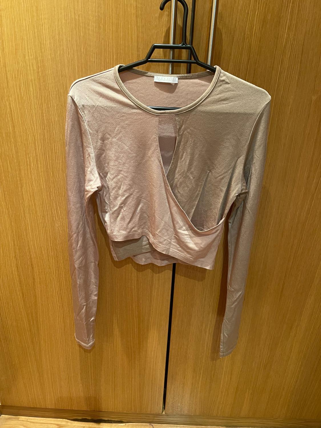 Front view of a beige long-sleeved blouse with an asymmetric neckline on a hanger.