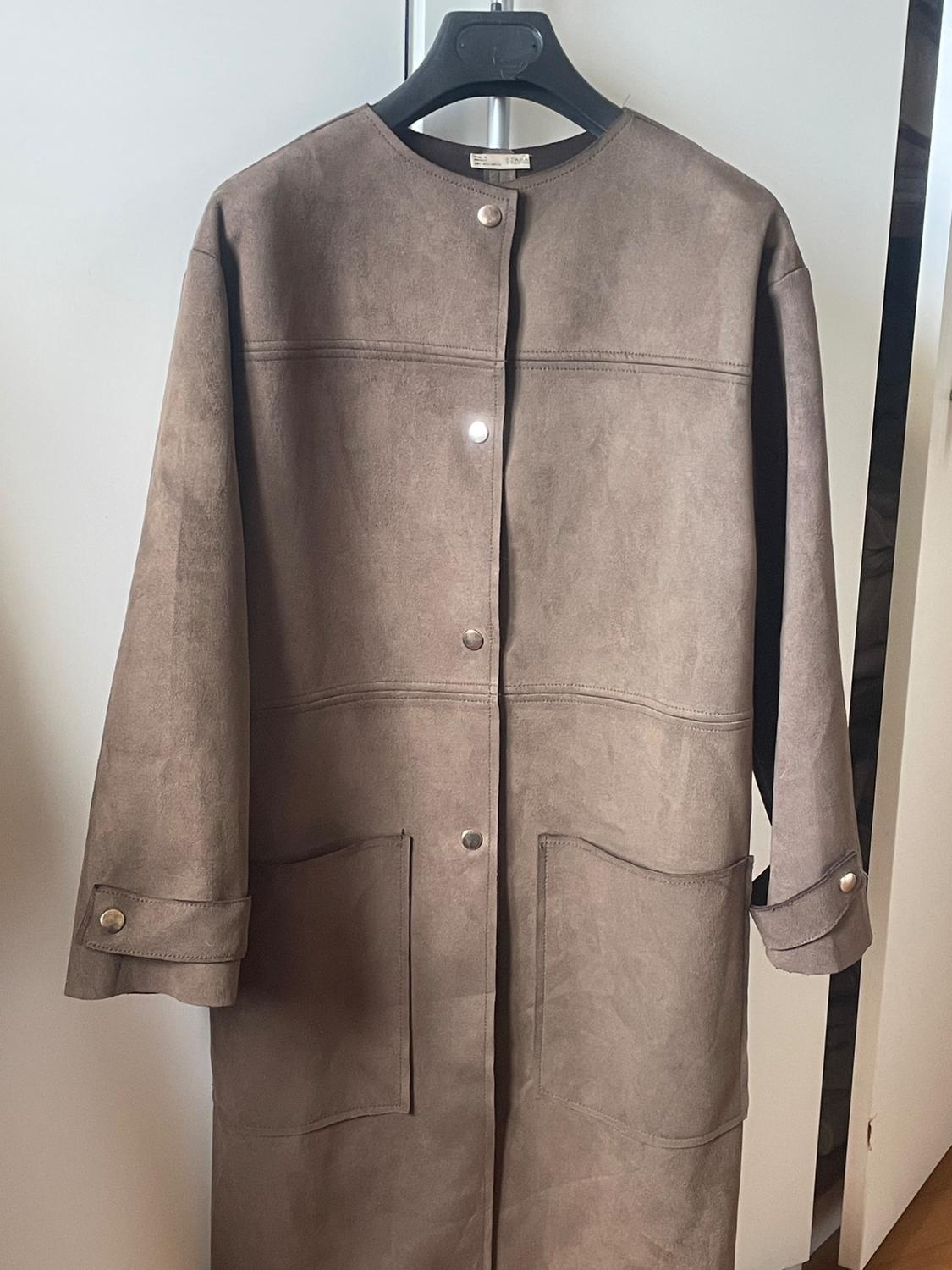 Light brown suede coat with metallic buttons and large pockets, hanging on a black hanger against a white background.