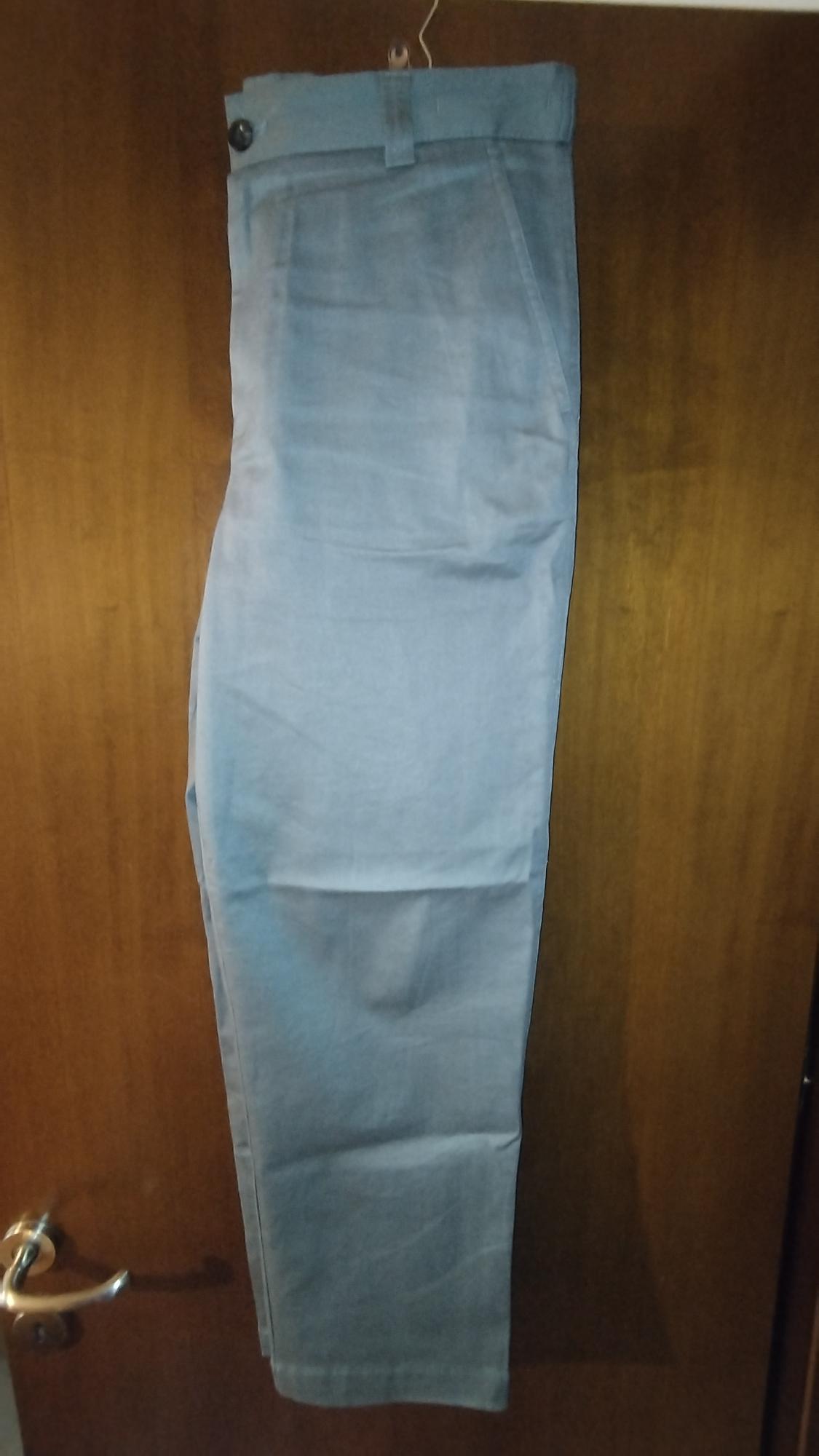 Light blue trousers hanging on a hanger over a wooden door. The trousers have a visible black button at the waist.