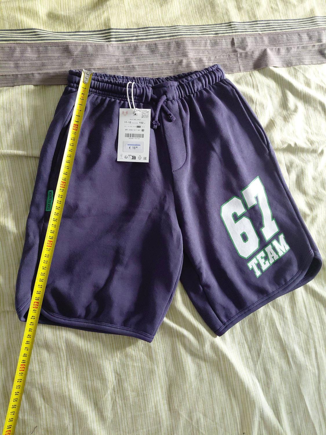 Dark purple sports shorts on striped fabric. A yellow tape measure is measuring them. They have the text ‘67 TEAM’ on the leg.