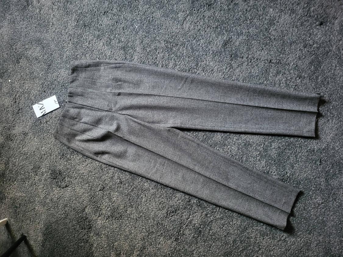 Grey fabric trousers on a grey carpet, with a visible label that says "ZARA".