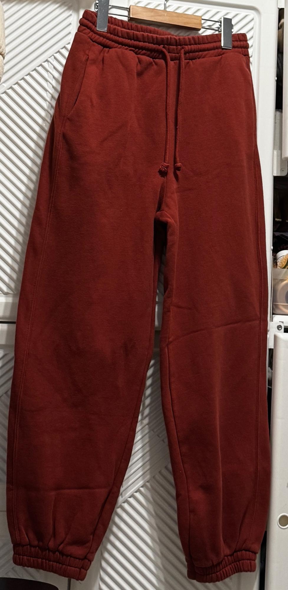 Front view of red tracksuit bottoms with elasticated waistband and side pockets.
