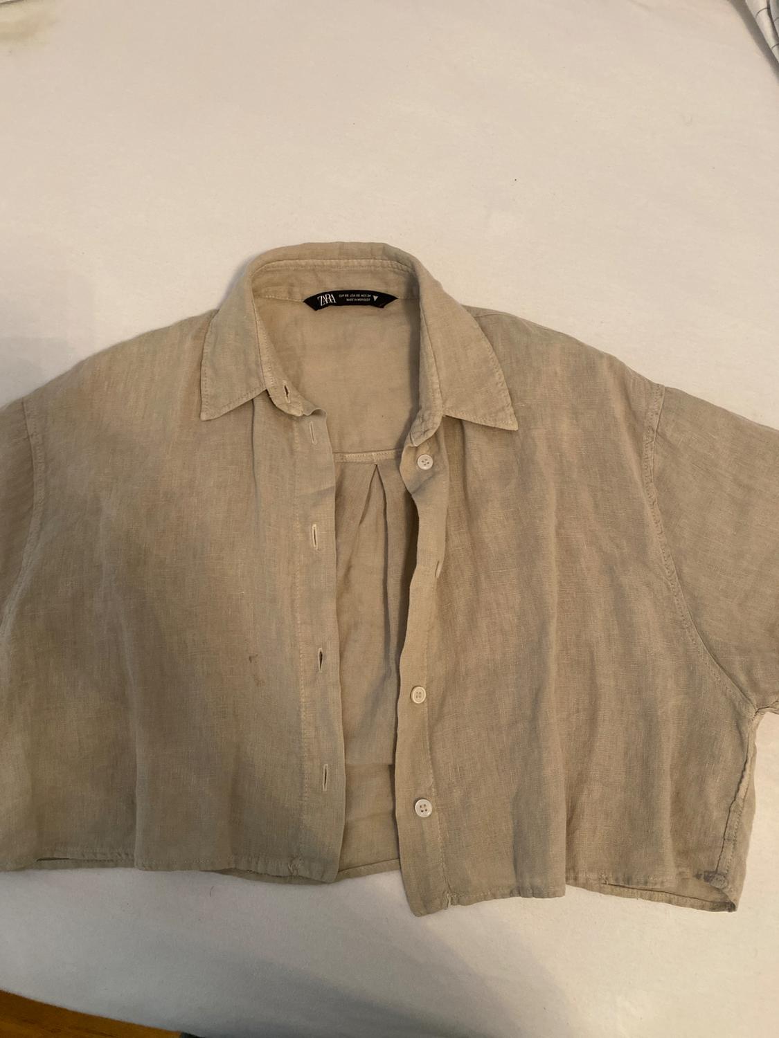 Beige short-sleeved button-up shirt, laid flat on a white sheet. Relaxed style. Label with the text ZARA.