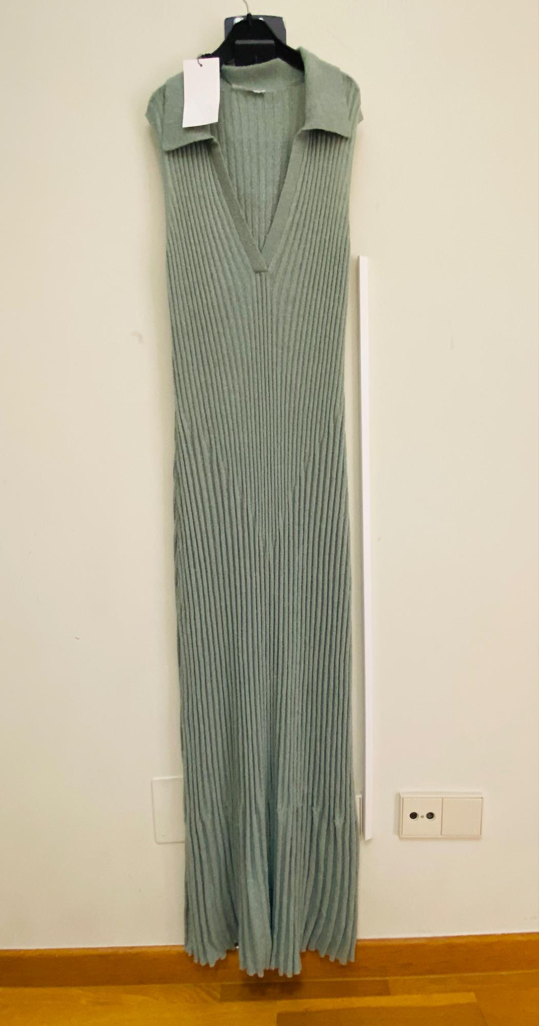 Green ribbed knit maxi dress with V-neck and sleeveless design, hanging on a black hanger against a white wall.