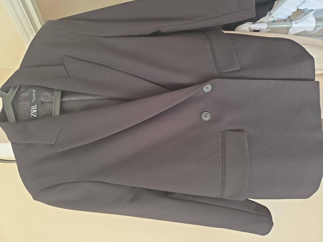 Black suit jacket hanging on a hanger, with two buttons and a visible pocket. Zara label inside.