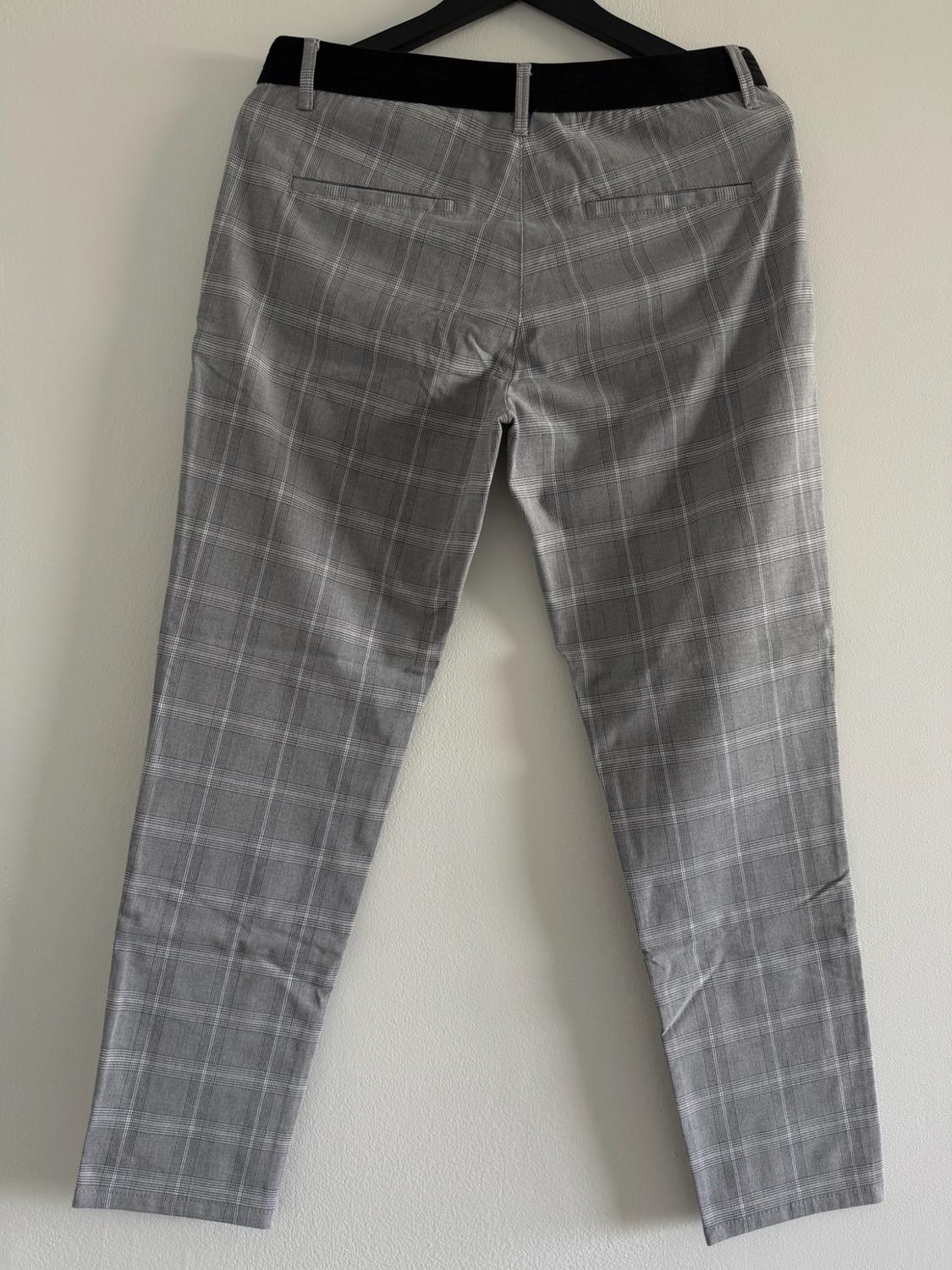 Back view of gray plaid pants with a black waistband, hanging on a hanger against a white wall.