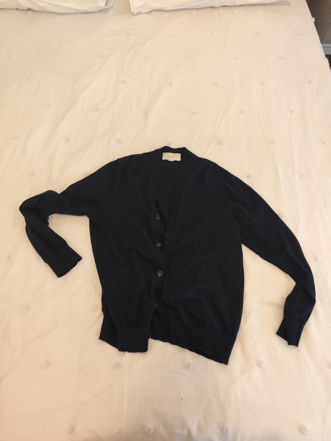 Black long-sleeved button-up cardigan, placed on a bed with a white quilted bedspread.