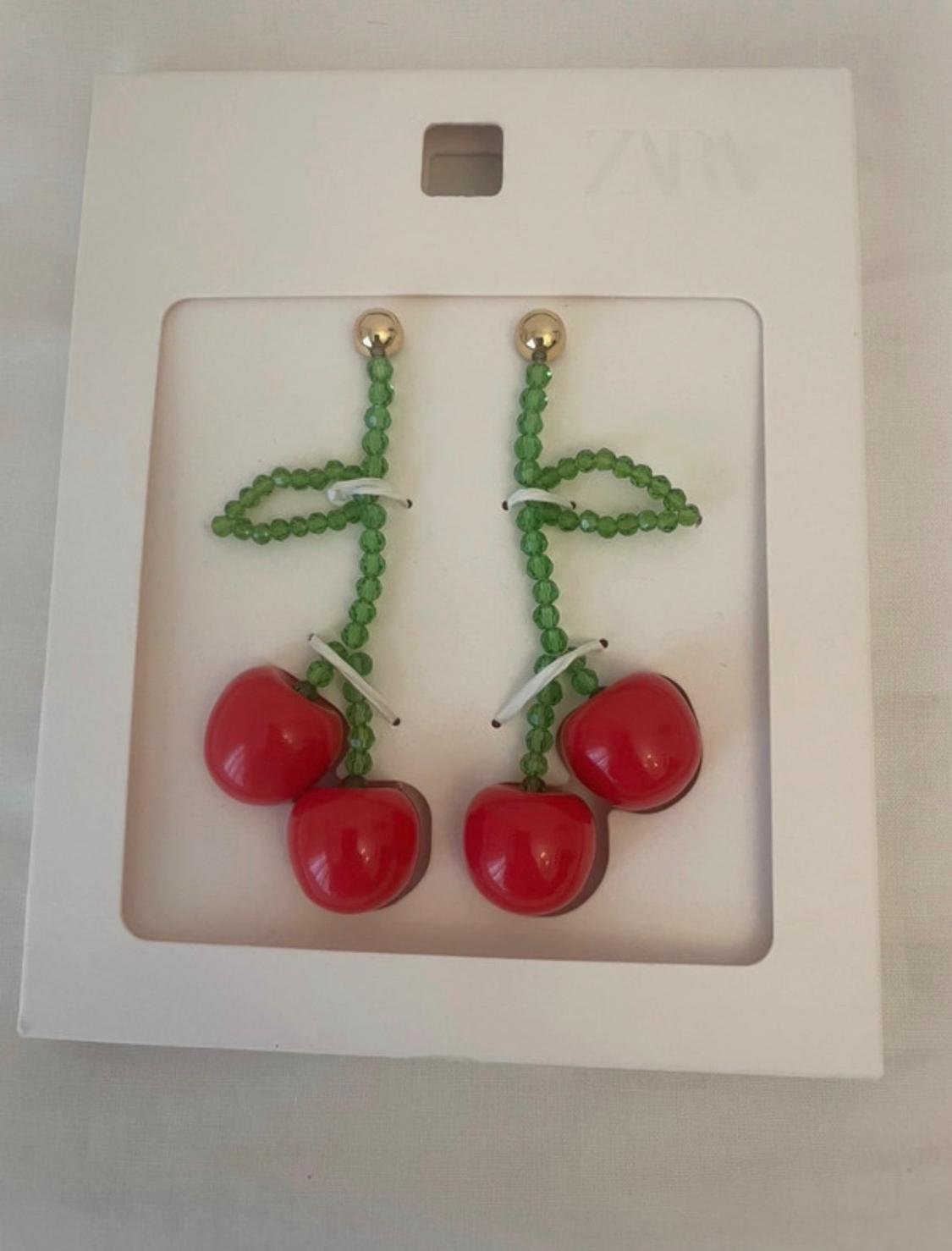 Cherry earrings with green beaded stems and shiny red fruits, presented on white card bearing the text ZARA.