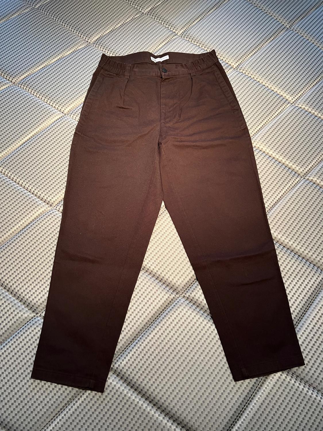 Dark brown trousers with an elasticated waist and button, placed on a light-coloured padded surface.