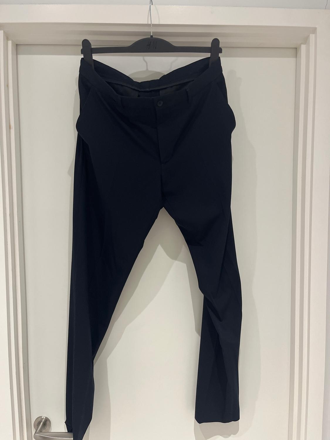 Black trousers hanging on a hanger over a white door. The hanger has the "H&M" logo.