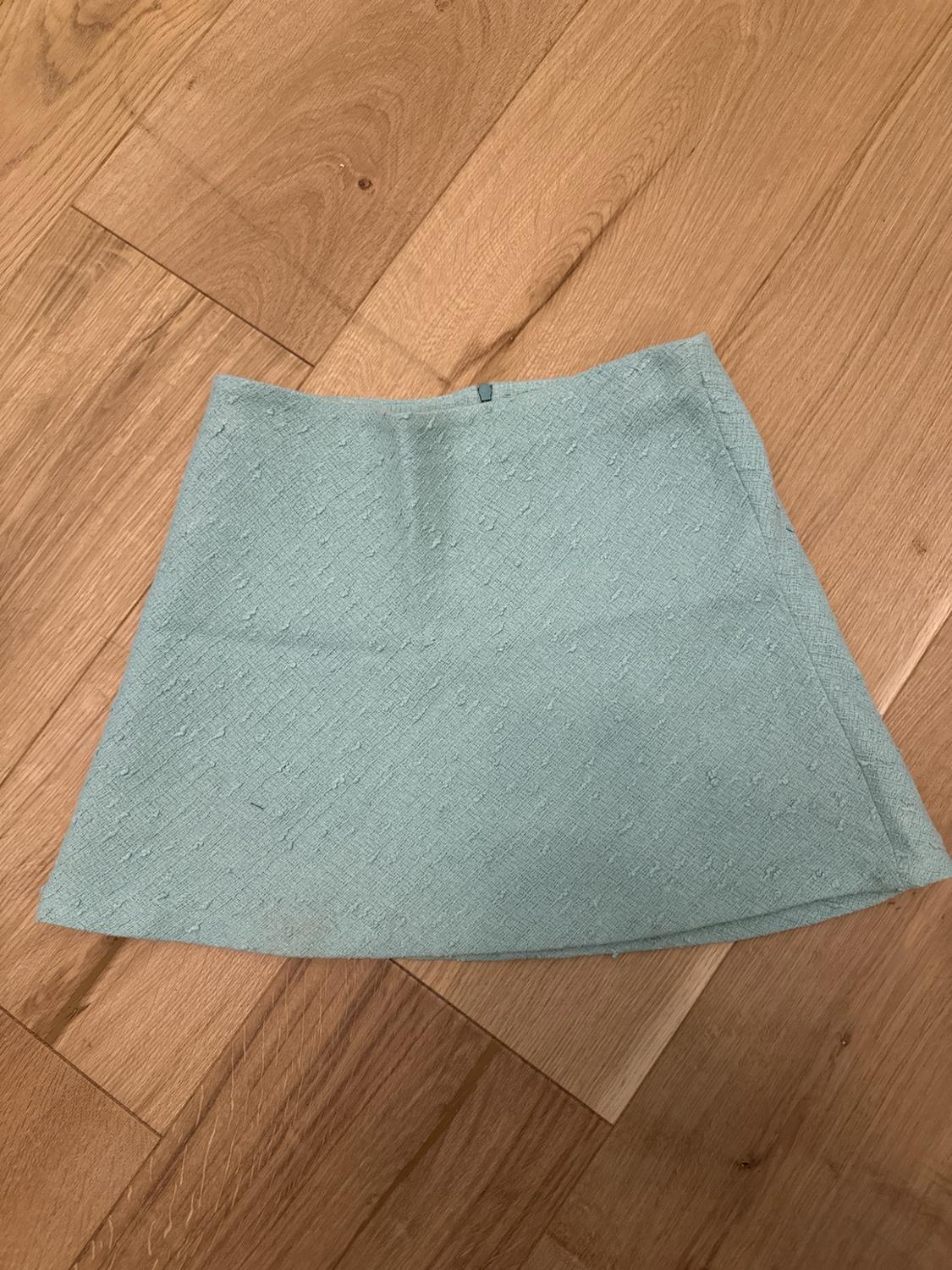 Light blue textured fabric mini skirt, photographed from above on a wooden floor.