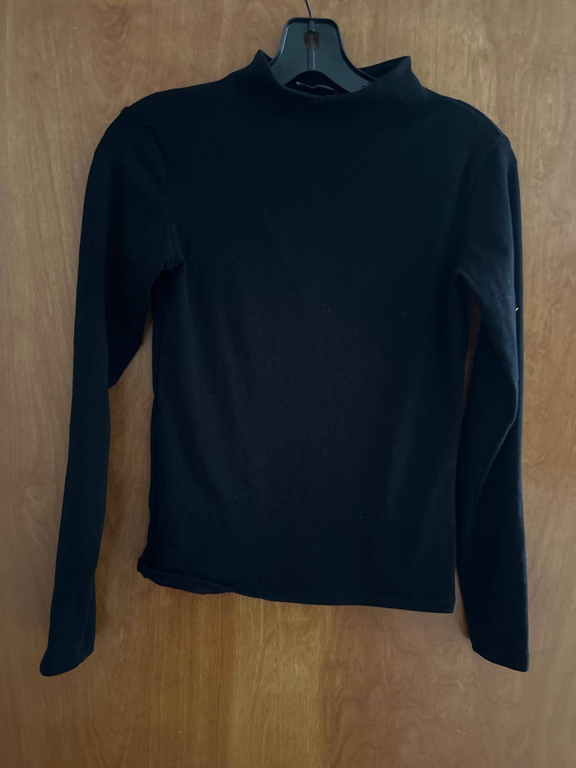 Black long-sleeved roll-neck top hanging on a black hanger in front of a wooden door. Casual and minimalist style.