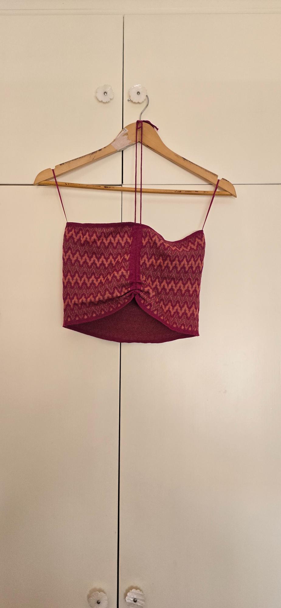 Maroon halter-neck cropped top with a zigzag print and central ruching, hanging on a wooden hanger against a white wardrobe.