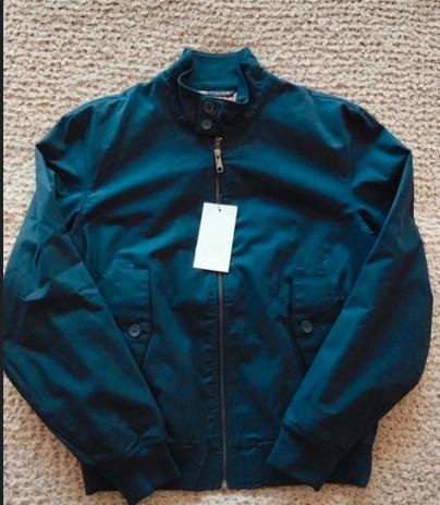 Dark blue jacket with zip and white hanging tag, on a beige rug.