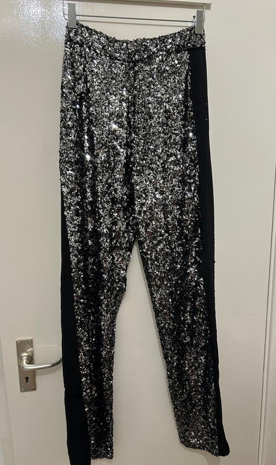 Trousers hung with silver sequins and black side panels, on a white door with a silver handle.