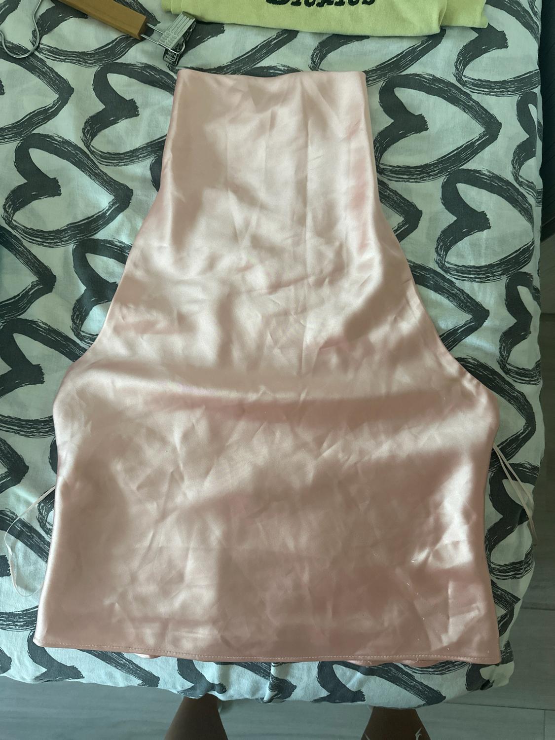 Satin pink top on a sheet with a heart print. Relaxed-style image with a wooden hanger at the top.