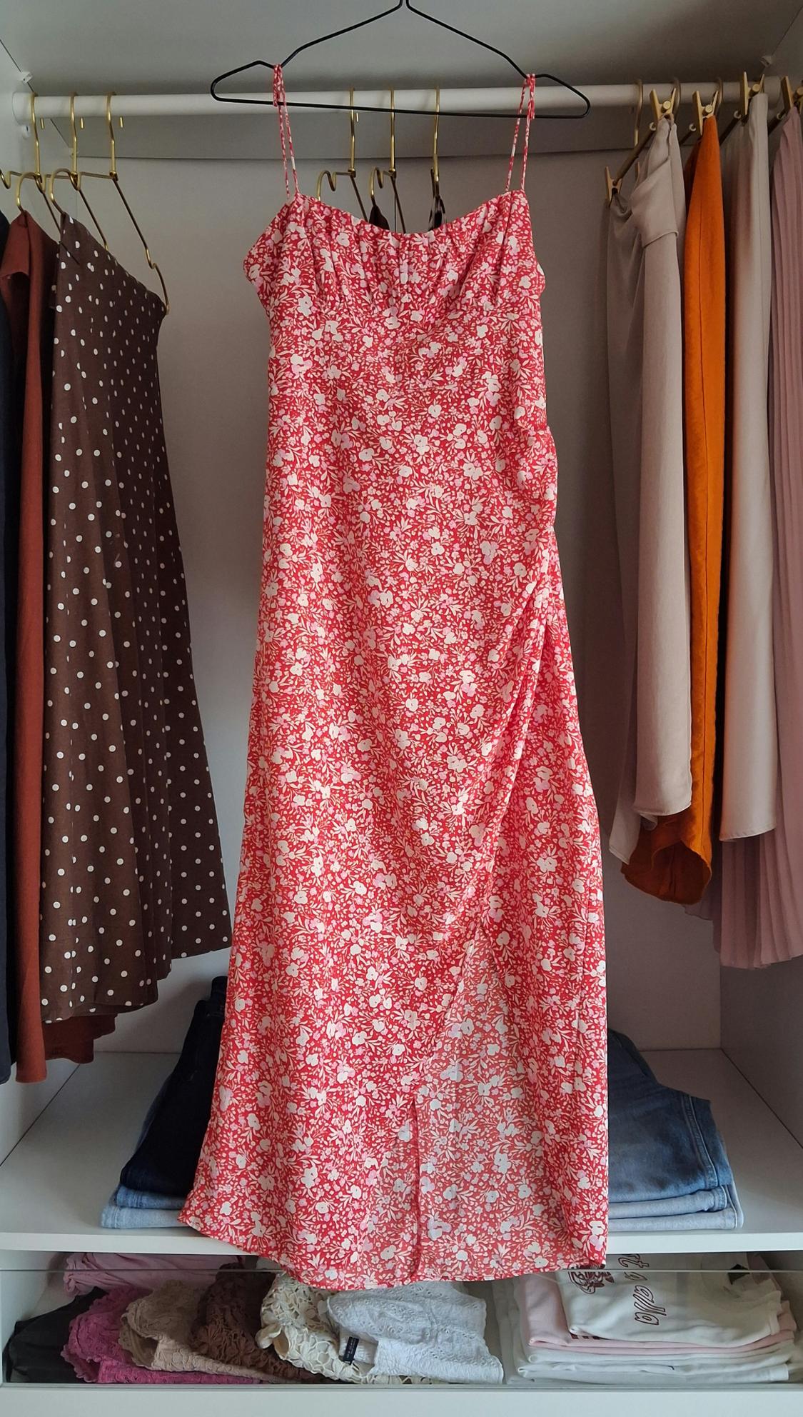 Red floral print strappy dress with a slit, hanging in a wardrobe. Underneath, folded clothes with the text la vita è bella.