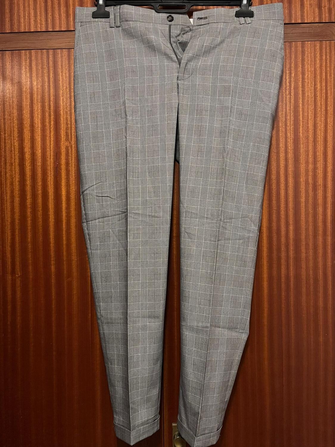 Grey checked trousers hanging on a hanger against a brown wooden background.