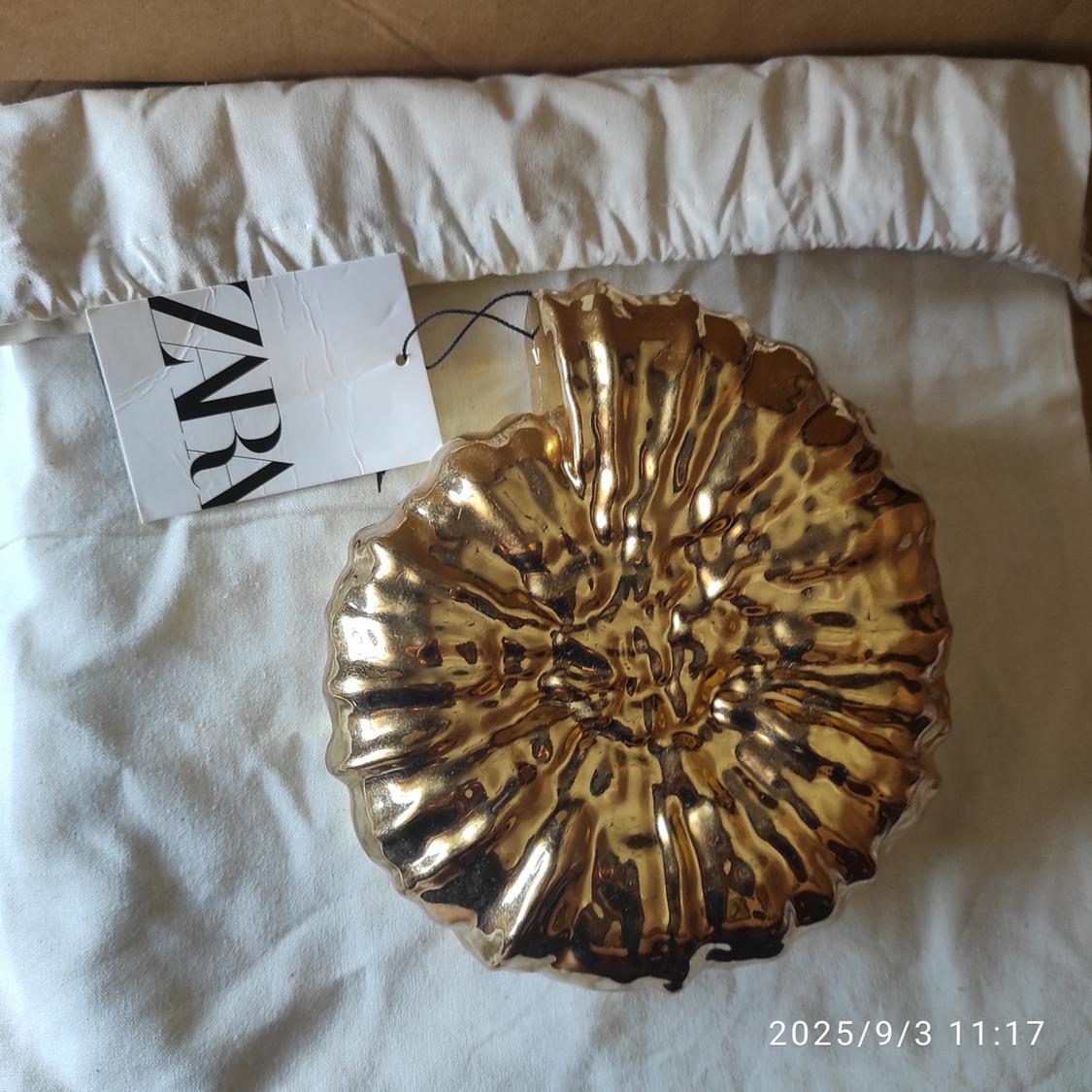 Decorative gold plate on white fabric with Zara label. Date on image: 2025/9/3 11:17.