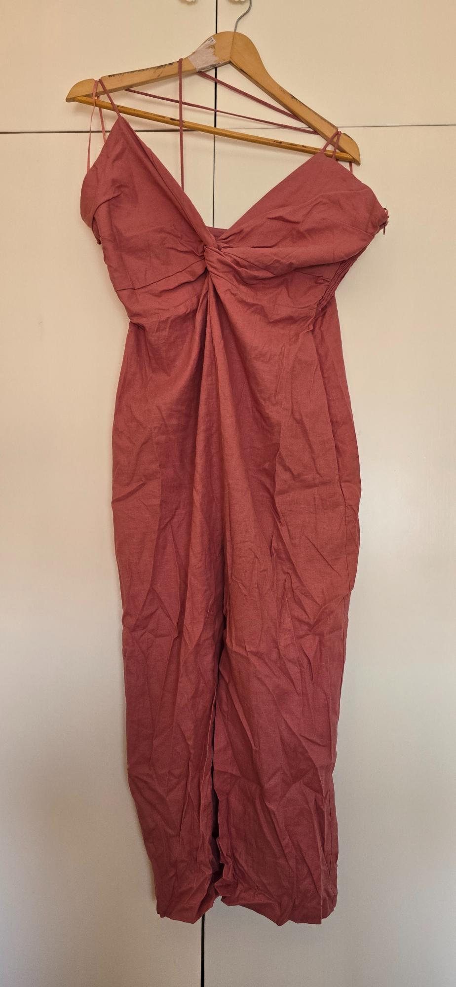 Pink camisole with a knot on the neckline, hanging on a wooden hanger against a white background.