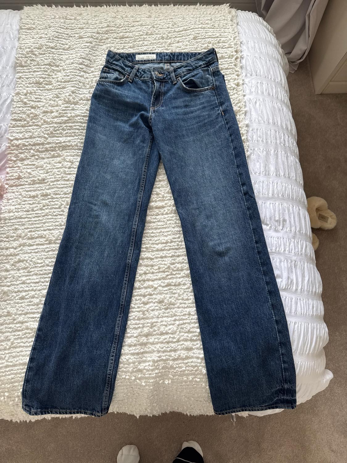 Blue jeans laid out on a bed with a textured white blanket. Relaxed atmosphere.