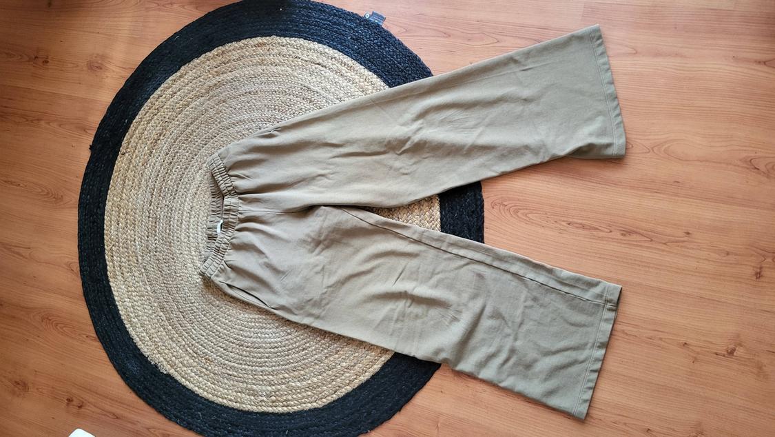 Beige wide-leg trousers with an elasticated waist, placed on a circular jute rug on a light wooden floor.