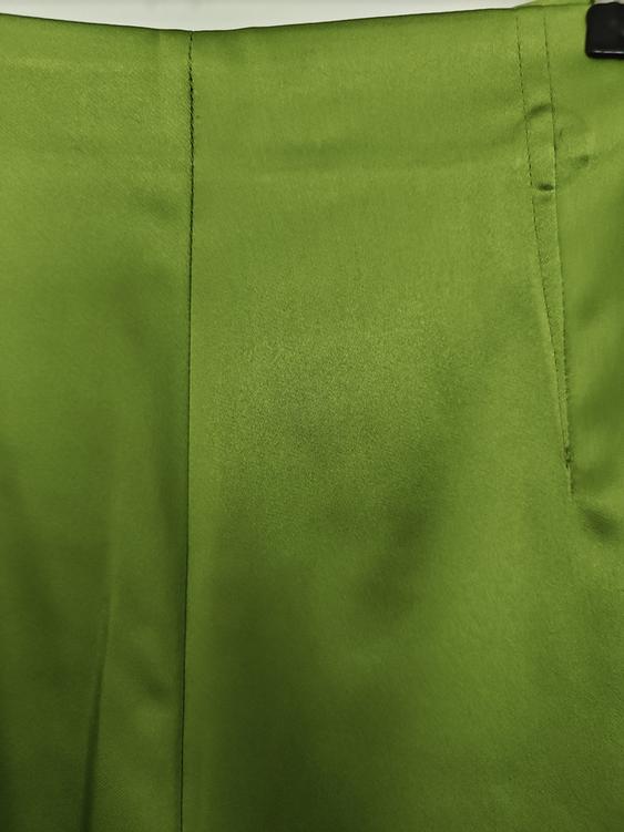 Close-up of a plain green fabric with a satin texture, showing vertical stitching and a side pocket.