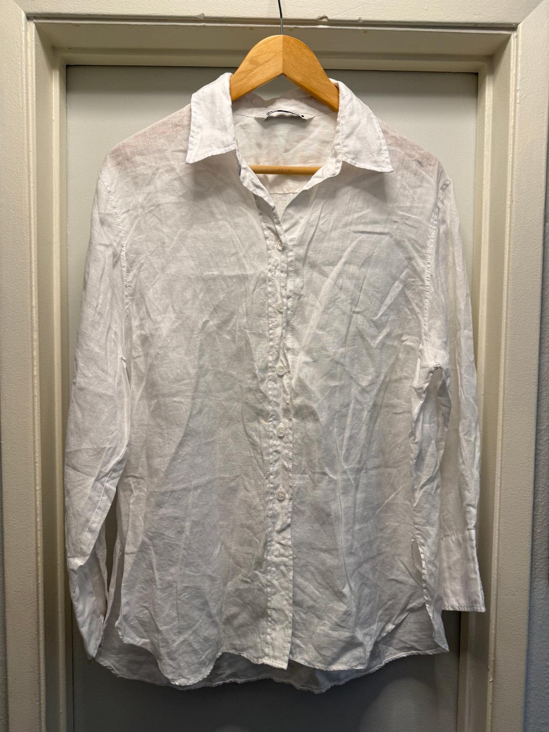 Wrinkled white long-sleeved shirt hanging on a wooden hanger over a white door.