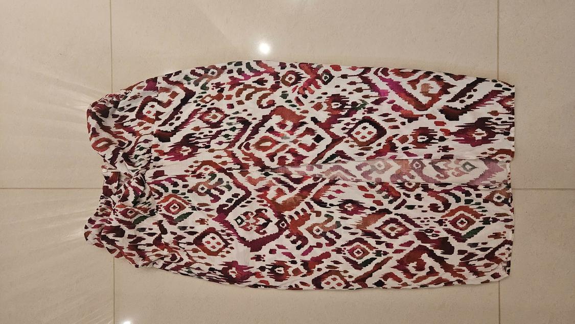 White skirt with a geometric print in shades of maroon and brown, with a front slit, laid out on a light-tiled floor.