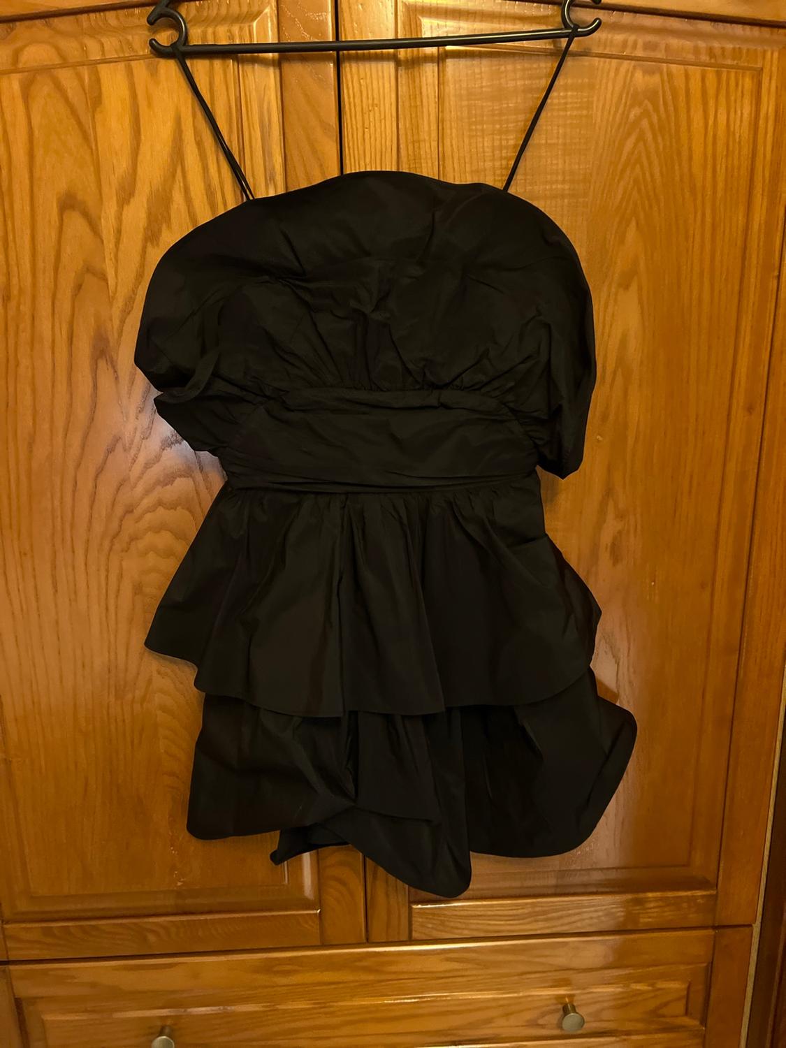 Short black dress with puffed sleeves and frills, hanging on a hanger in front of a wooden wardrobe. Relaxed atmosphere.
