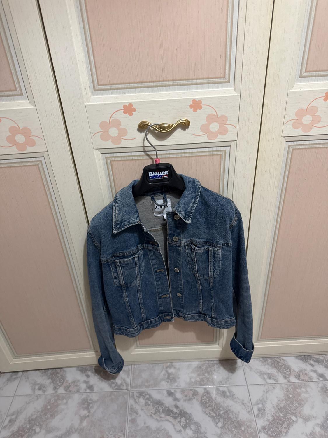 Blue denim jacket hanging in a white and pink wardrobe with flowers. Visible text: Blauer on the hanger and ZARA on the label.