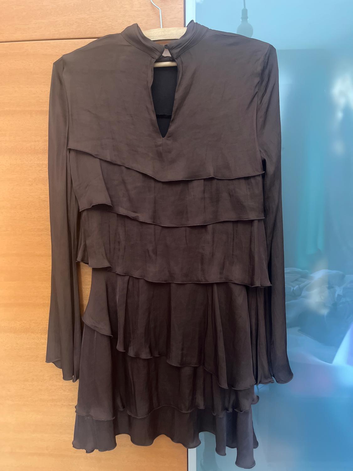 Dark brown, long-sleeved mini dress with a high neck, front slit, and layered ruffles, hanging on a wooden hanger.