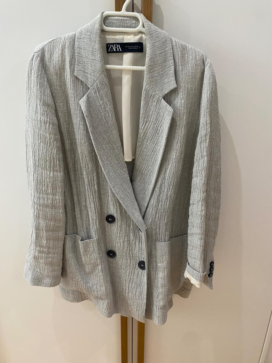 Textured grey double-breasted jacket hanging on a white hanger. Visible label with the text "ZARA".