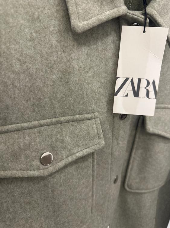 Grey coat with lapel and pocket with metallic button. Swing tag with the text "ZARA".