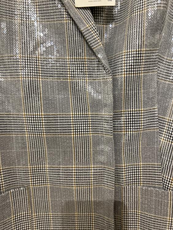 Jacket fabric with a check print in grey and beige tones, decorated with shimmering sequins. Visible label with text "www.zara.com".
