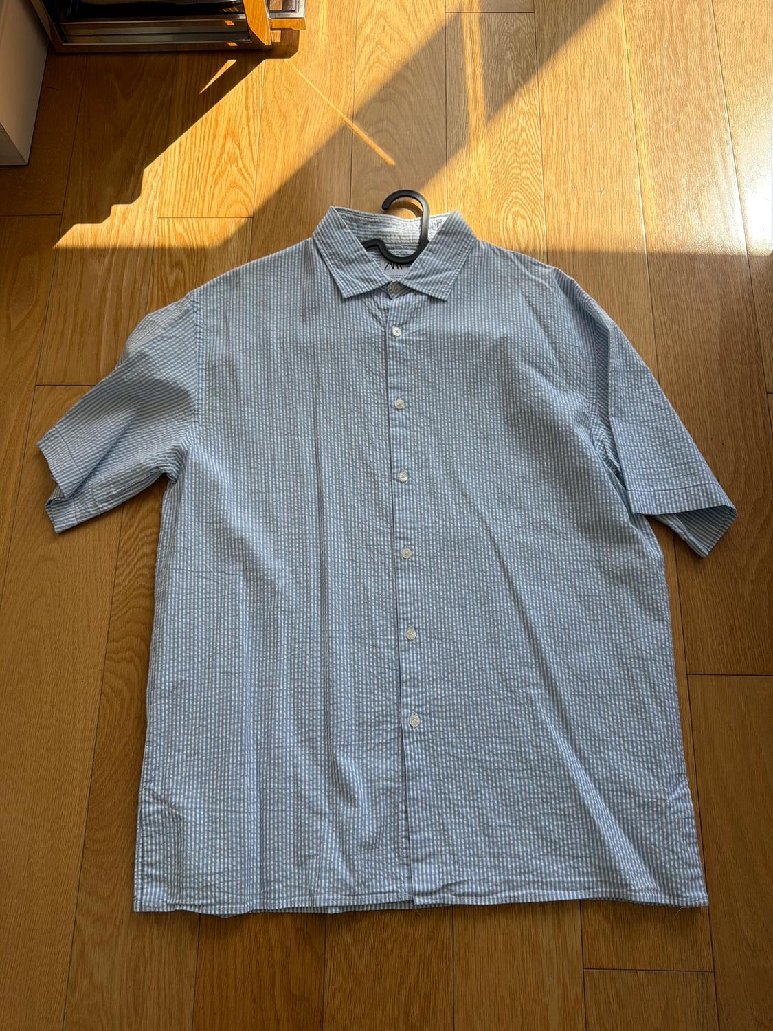 Blue and white striped short-sleeve shirt on a wooden floor, illuminated by sunlight.