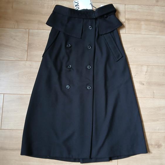 Black double-breasted skirt on a light wooden floor. Visible label at the top.