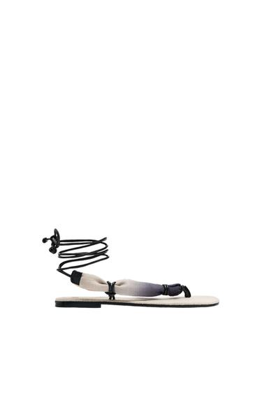 Side view of a black flat sandal with straps and a knot detail on the vamp.