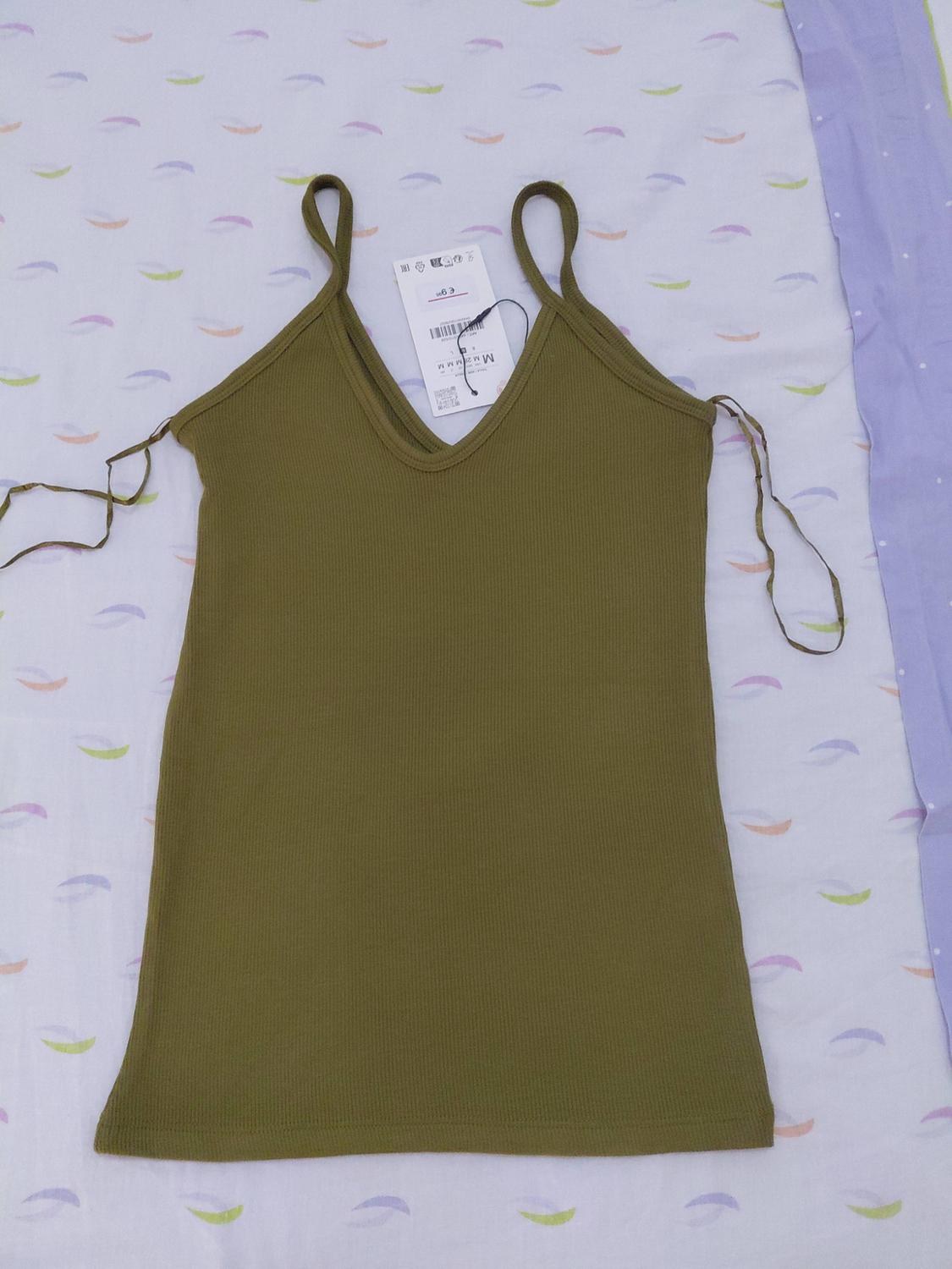 Olive-green ribbed camisole with straps, a V-neck and side ties, on white fabric with a pastel print and lilac fabric with polka dots.
